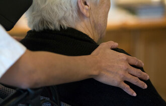 Bildet viser en eldre mann sett bakfra, der en omsorgsfull hånd ligger på skulderen hans.