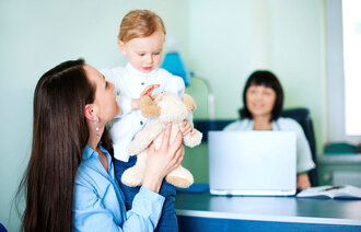 Bildet viser en mor som løfter sitt barn. De sitter foran pulten til helsesøsteren, som skimtes i bakgrunnen.