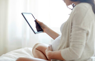 Bildet viser en gravid kvinne som sitter i en seng og ser på et nettbrett
