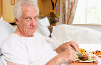 Bildet viser en eldre mann i en sykehusseng som har fått servert et måltid mat på sengen.