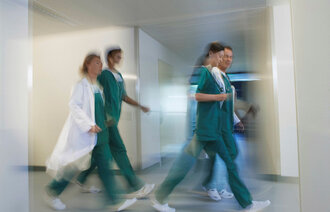 Bildet viser fire sykepleiere som går raskt gjennom en gang, på et uskarpt bilde.