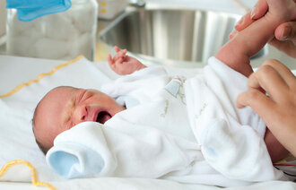 Bildet viser en nyfødt baby som gråter idet hen får skiftet bleie