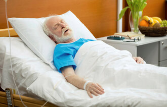 Bildet viser en eldre, syk mann i sengen på sykehus.