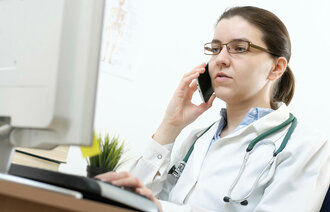Bildet viser en sykepleier som ringer til en pasient. Hun sitter foran PC-en.