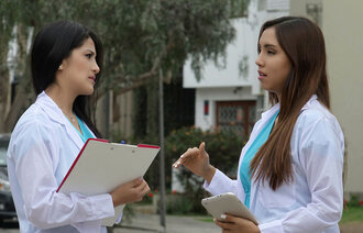 Bildet viser to unge kvinnelige sykepleiere som står ute og snakker sammen