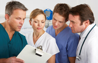 Bildet viser sykepleiere og leger som står og snakker sammen over en clipboard. Det er både menn og kvinner blant de fire.