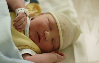 Bildet viser en nyfødt baby påkledd i sengen.