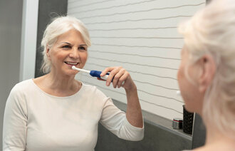 Bildet viser en eldre kvinne som pusser tennene med en elektrisk tannbørste