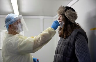 Bildet viser testpersonell som stikker en testpinne opp i nesen på en kvinne.