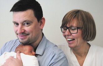Bildet viser nyfødte Oscar i armene til pappa Alexander Perez, med spesialsykepleier Inger Kopland bak.