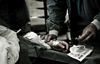 Bildet viser en hånd som holder en kanyle på operasjonsstuen.