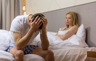 Illustrasjonsfoto av mann og kvinne som sitter i sengen. Mannen er tydelig frustrert.