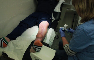 Sykepleier som utfører sårstell på en innsatt. Bildet viser en sykepleier som utfører sårstell på en innsatt.