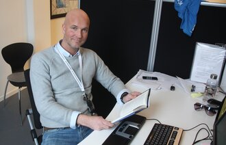 Bildet viser Jan-Erik Vik som sitter foran en datamaskin med bok i hånden.