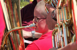 Nærbilde av gutt med kort hår og rød t-skjorte som spiller tuba i messingorkester