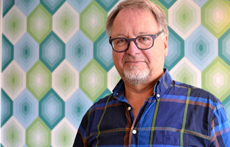 Forfatter Bengt-Ole Nordström står foran en fargerik og mønstrete vegg og ser i kamera,