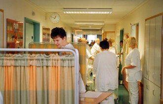 Bildet viser en sykehuskorridor med senger og mange pleiere.