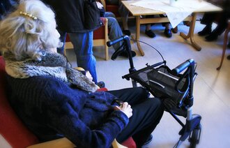 Eldre dame som sitter med ryggen til inne på et sykehjem