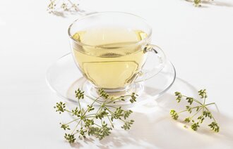 Bildet viser en gjennomsiktig kopp med te, omgitt av fennikel.