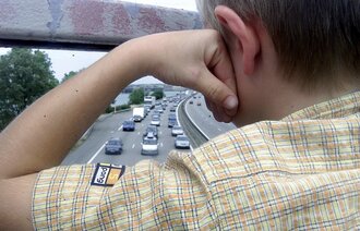 Ung gutt som står og skuer ut over motorveien fra bru