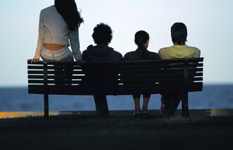 Fire ungdommer som sitter på en benk med ryggen til kamera og ser utover