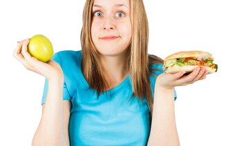 En jente holder en hamburger i ene hånden og ett eple i den andre. Valgets kval