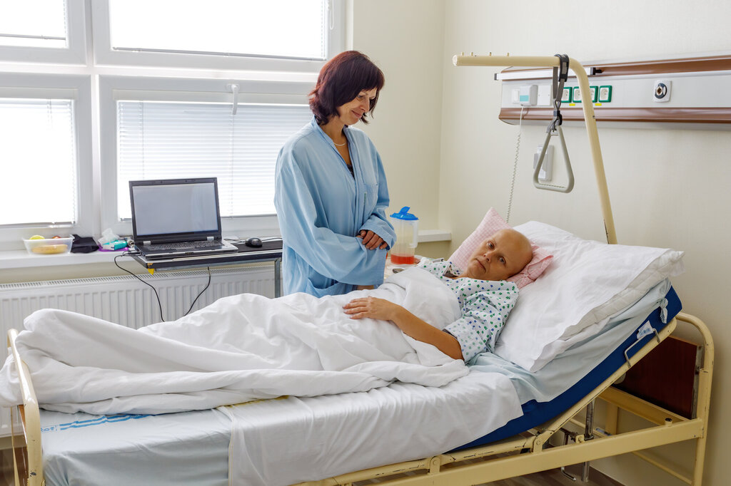 Bildet viser en kvinne som står ved sengen til en døende kvinnelig kreftpasient
