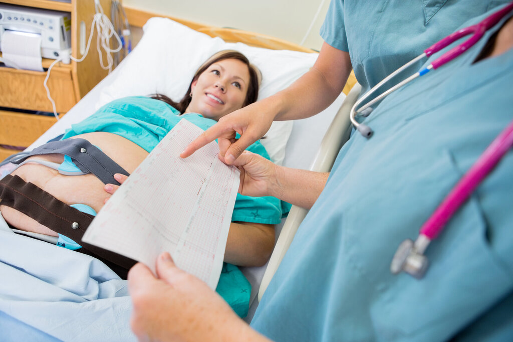 Bildet viser en høygravid kvinne som ligger i sengen og får ultralyd. To sykepleiere står ved siden av og diskuterer noe på et ark 