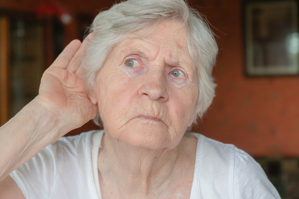 Bildet viser en eldre dame som har hånden bak øret for å lytte.