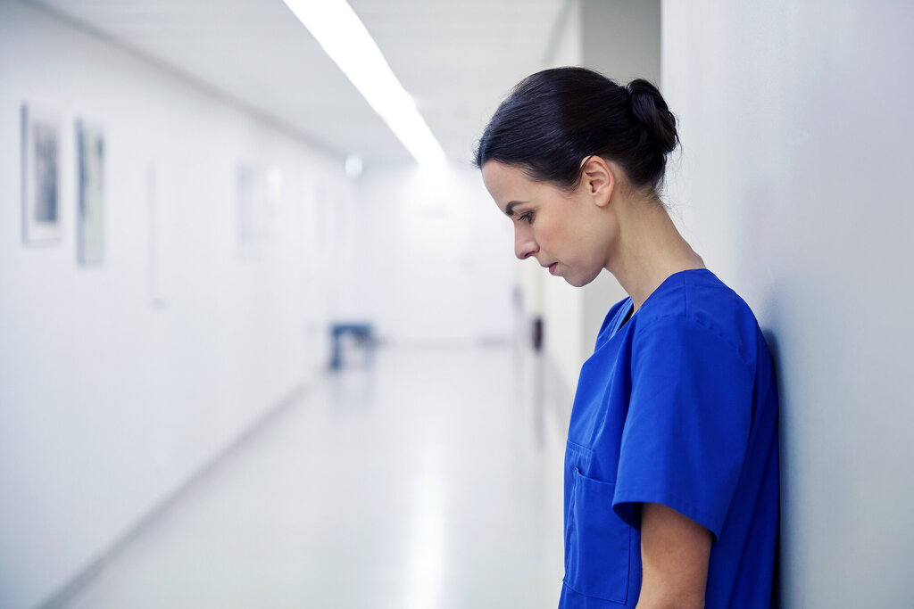 Bildet viser en sykepleier som står inntil en vegg. Hun er sliten