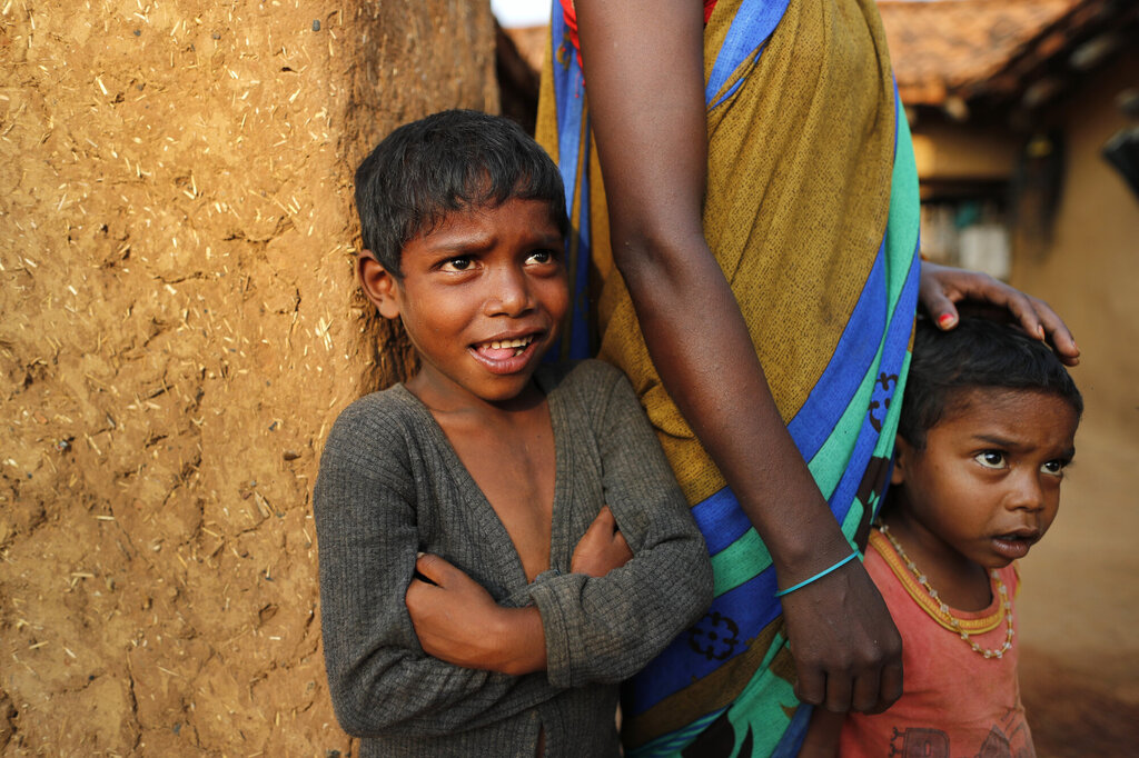 Bildet er fra India og viser to barn som står sammen med en voksen person og ser på helsearbeidere som overtaler eldre til å vaksinere seg mot korona