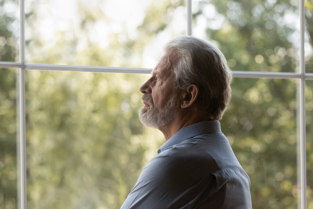 Bildet viser en eldre mann som titter ut av vinduet. Han ser tankefull og bekymret ut