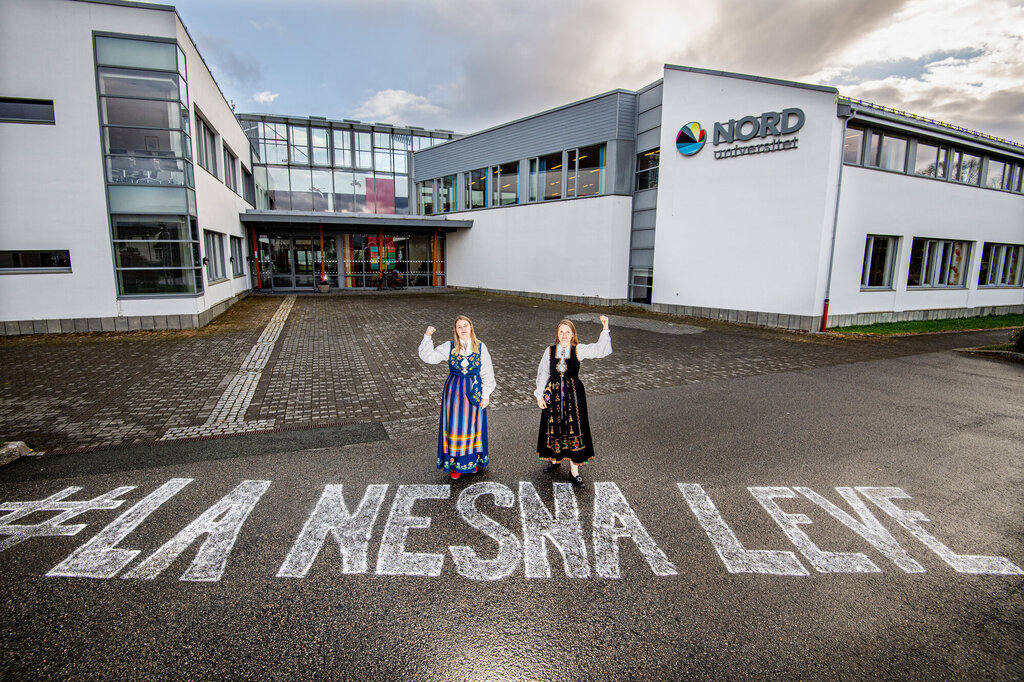 Bildet viser to bunadskledte mennesker utenfor høgskolen i Nesna, på bakken er det skrevet "La Nesna leve".