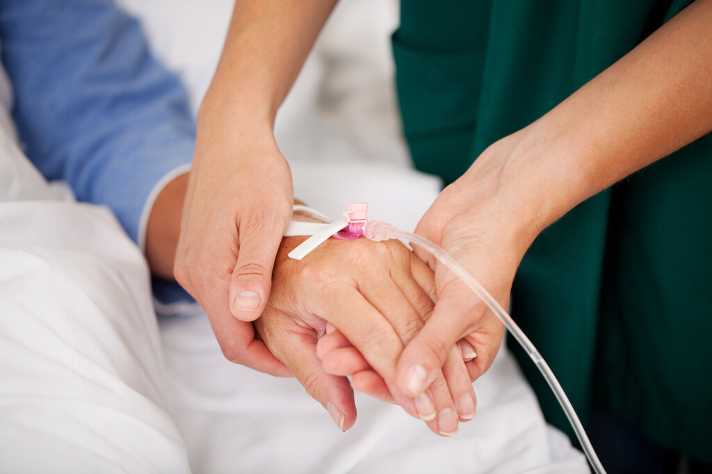 Bildet viser en sykepleier som holder hånden til en pasient. 
