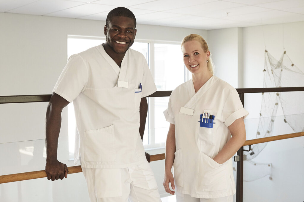 Bildet viser en mannlig og en kvinnelig sykepleier som smiler.