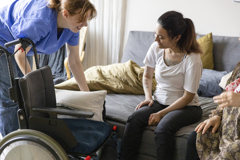 Bildet viser en sykepleier i hjemmetjenesten som hjelper en rullestolbruker