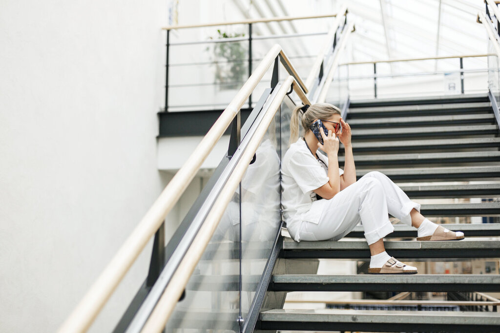 Bildet viser en sykepleier som sitter i en trapp, snakker i telefonen og ser sliten ut