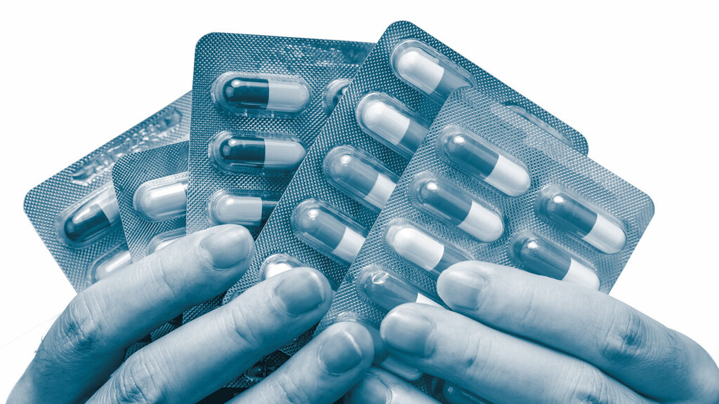 The photo shows hands holding various pills and tablets