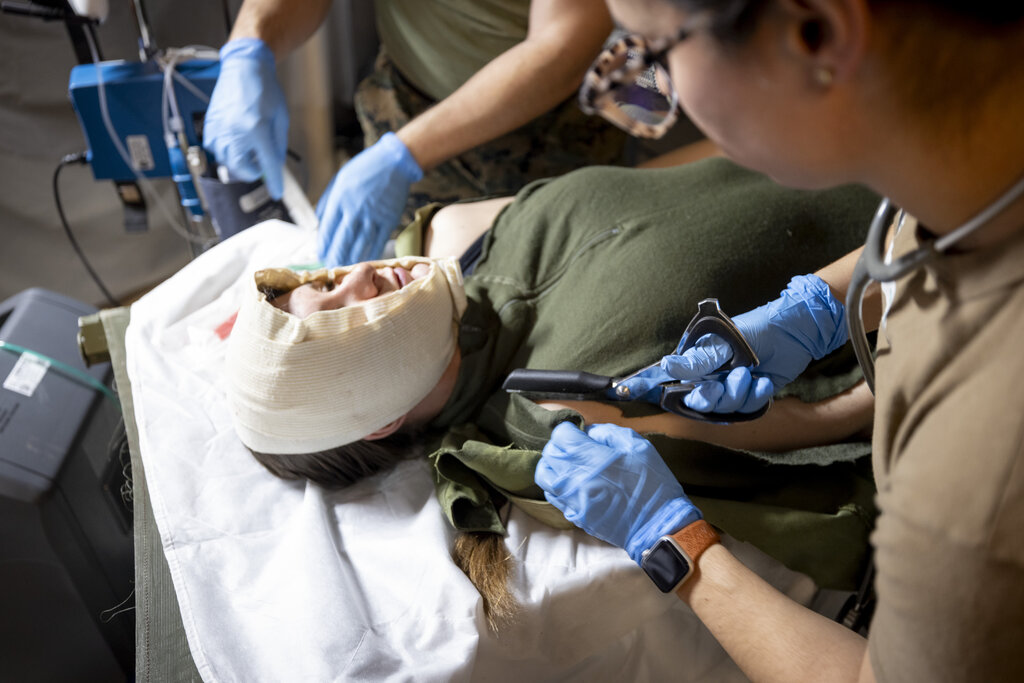 Bildet viser en sanitetssoldat som klipper opp klærne til en såret soldat.