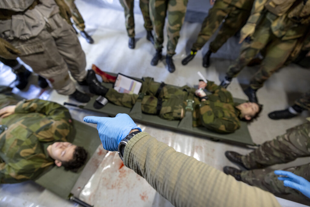Bildet viser en hanskekledd hånd som peker på sårede soldater.
