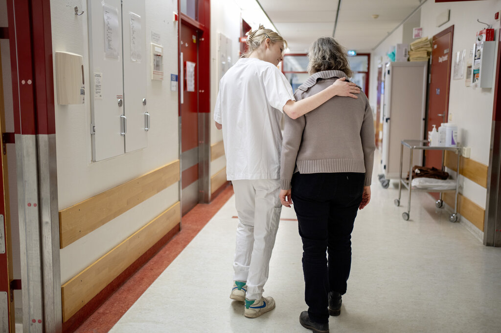 Bildet viser en sykepleier som støtter en pasient i en sykehusgang