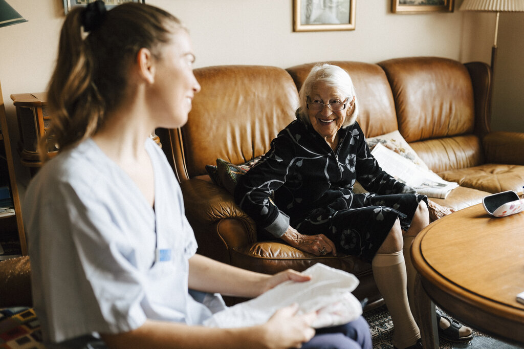 Bildet viser en sykepleier i hjemmetjenesten som snakker med en eldre pasient