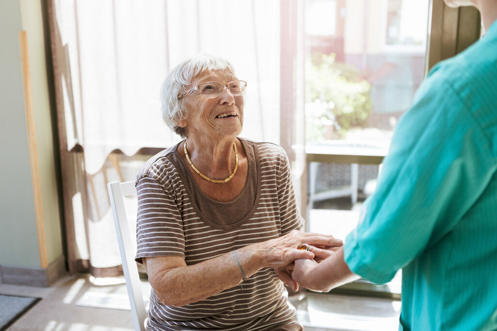 Bildet viser en hjemmeboende eldre kvinne som smiler til en sykepleier.