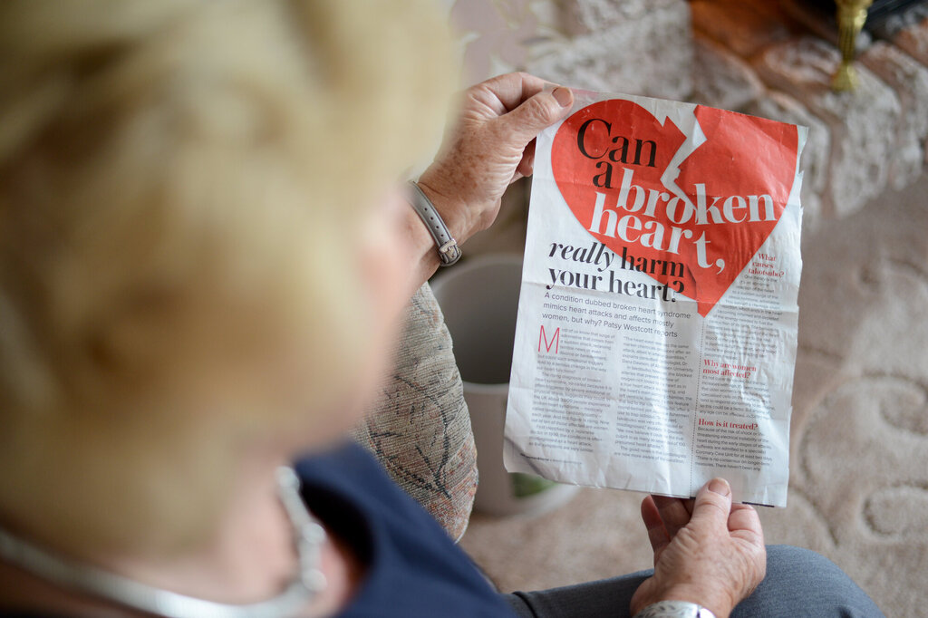 Bildet viser en eldre kvinne som holder opp et avisutklipp hvor det står "can a broken heart really harm your heart?"