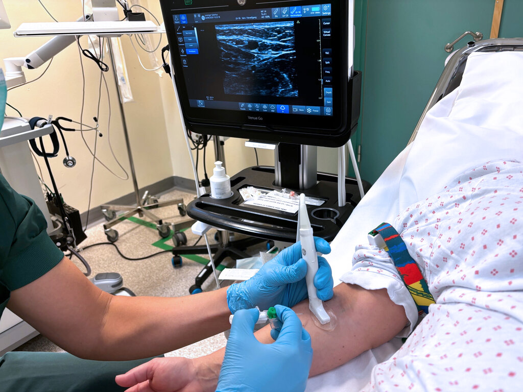 The photo shows a nurse using ultrasound to locate a vein before catheterisation