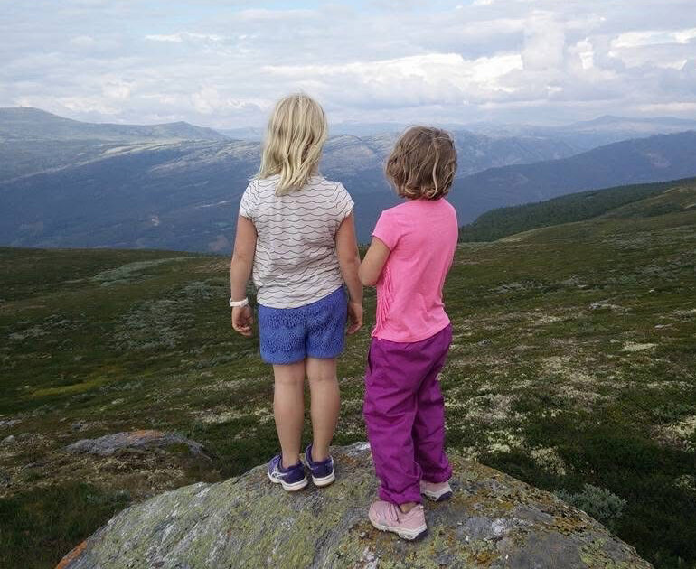 Bildet viser to små jenter på en fjelltopp. De ser utover landskapet.