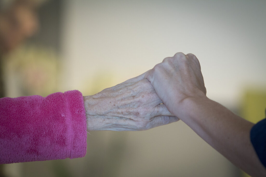Bilde av en sykepleier som holder en eldre kvinne i hånden.
