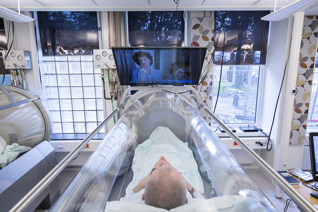 Bildet viser en person som får behandling i trykkammer mens vedkommende ser på TV på en skjerm over kammeret.