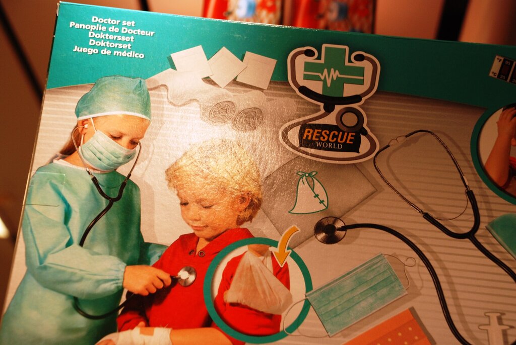 Bildet viser boksen til et doktorlekesett der en jentelege undersøker en guttepasient.