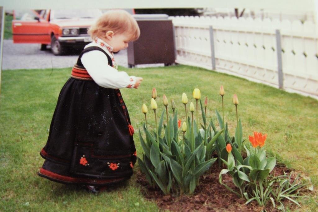 Bildet viser Lillian Elise Esborg Bergane som liten i bunad og som ser på tulipaner i knopp.